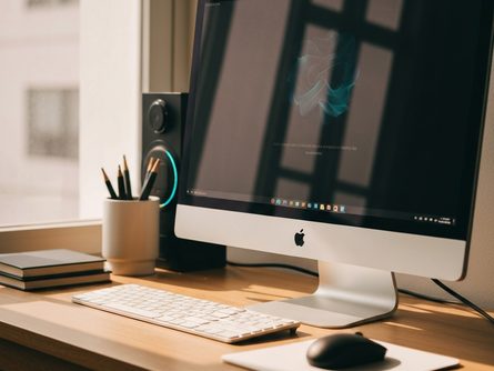 밝은 햇살이 드는 책상 위에 놓인 게이밍 키보드와 마우스, 흐릿한 모니터 배경