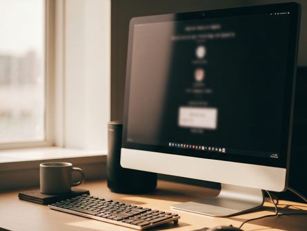 손으로 잡은 스마트폰과 무선 마우스·키보드, 흐릿한 모니터 배경